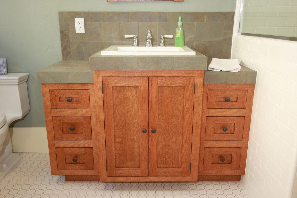Remodeled bathroom with a wooden vanity, stone countertop and tiled backsplash